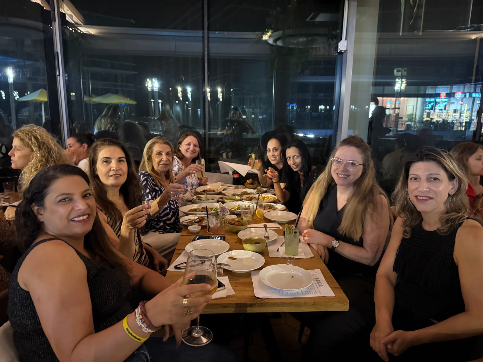 נשים סביב שולחן ארוך מרימות כוסית ומחייכות למצלמה